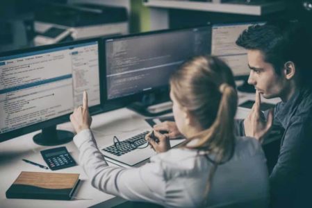 Workers reviewing code on computer screens.